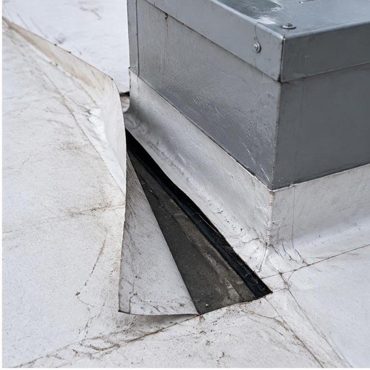 Open commercial roof membrane seam beside a rooftop curb