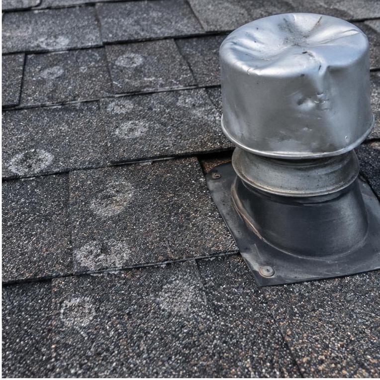 Hail marks on shingles beside a dented roof vent