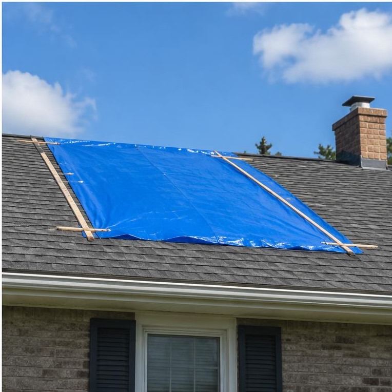 Temporary tarp secured over a storm-damaged roof opening